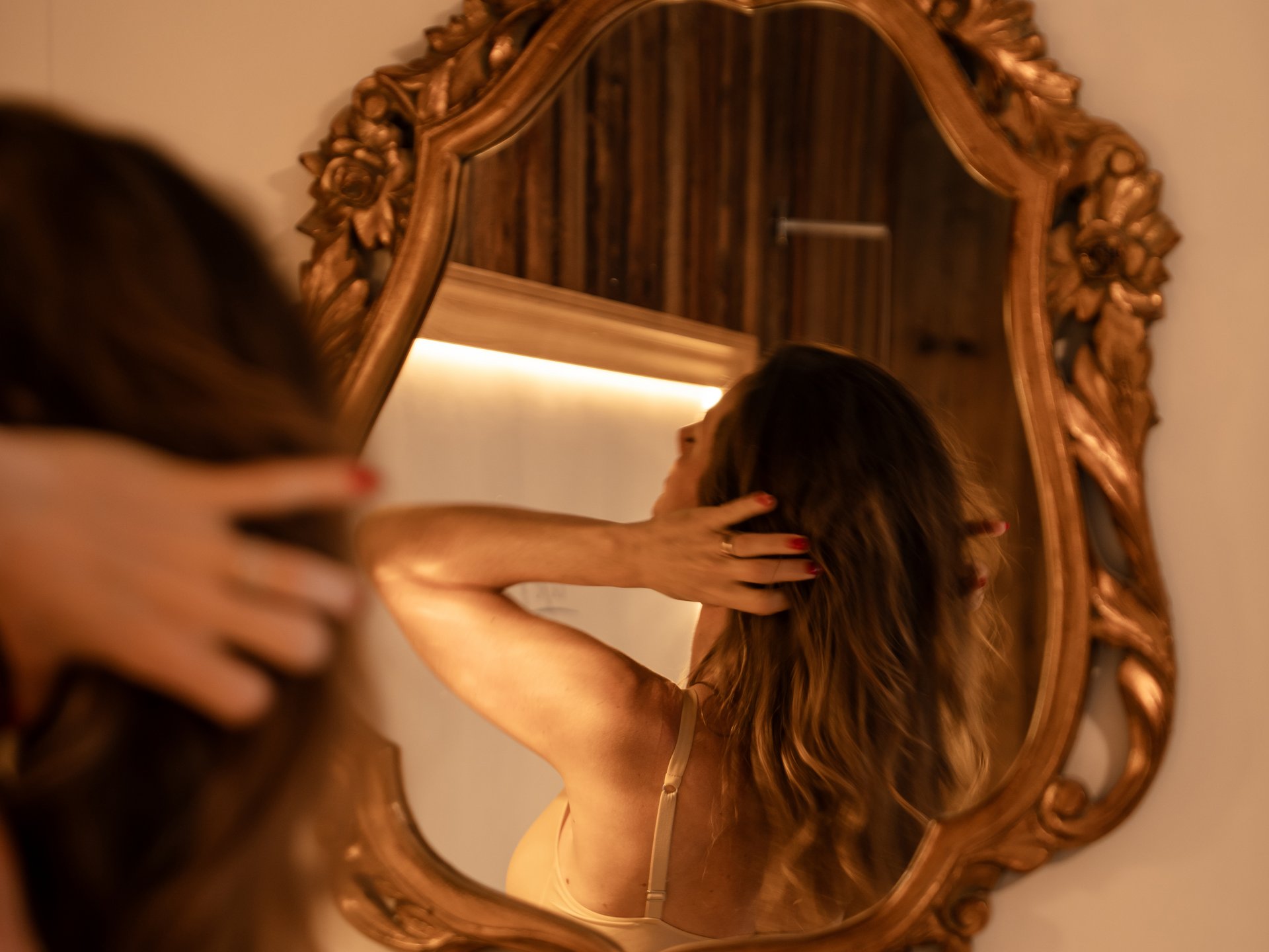 Wohlfühlurlaub im 5-Sterne-Hotel in Serfaus Frau betrachtet sich im verzierten Wandspiegel und berührt ihr Haar