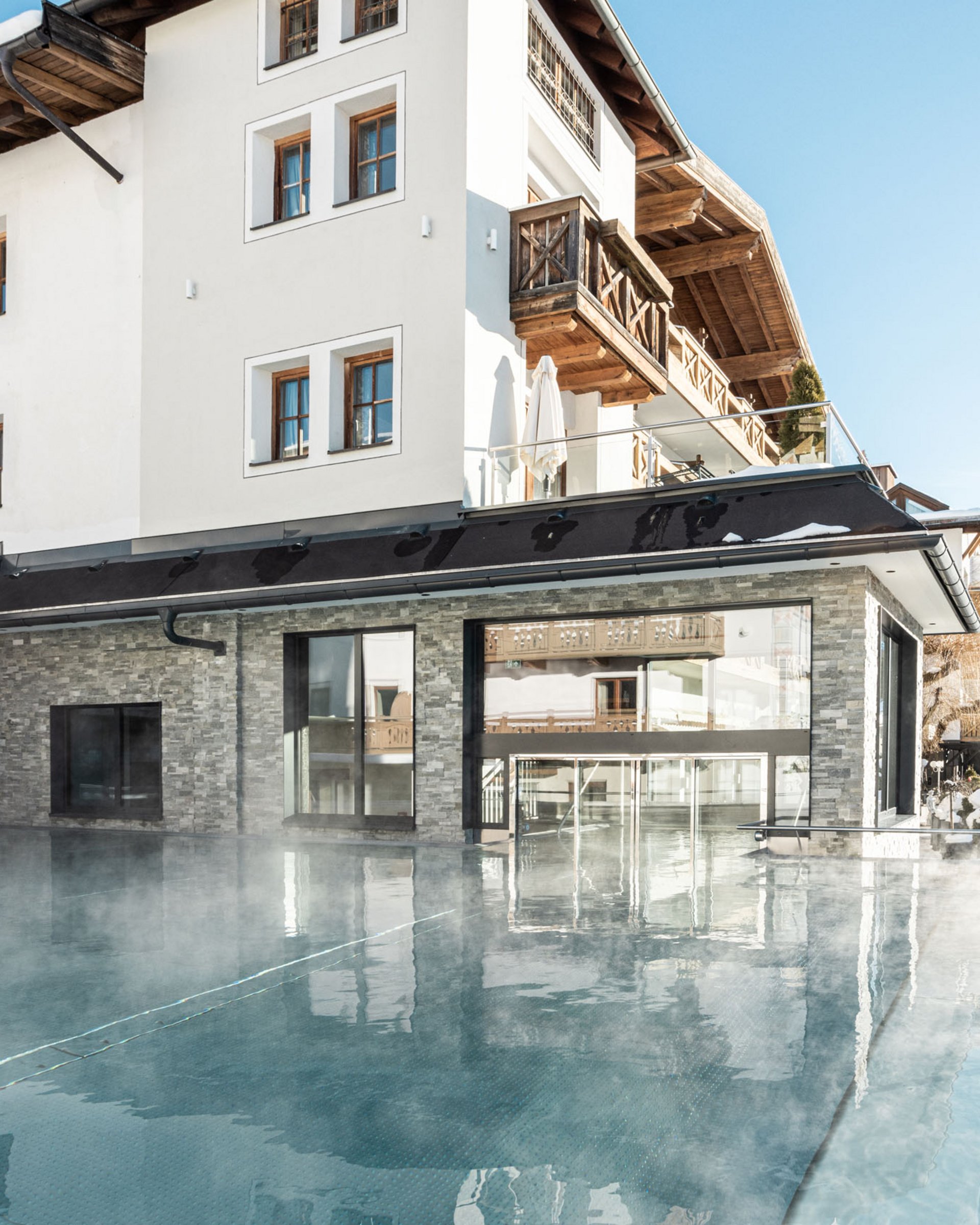 Wohlfühlurlaub im 5-Sterne-Hotel in Serfaus Außenpool mit Dampfwolken neben moderne Berghotel bei Schnee