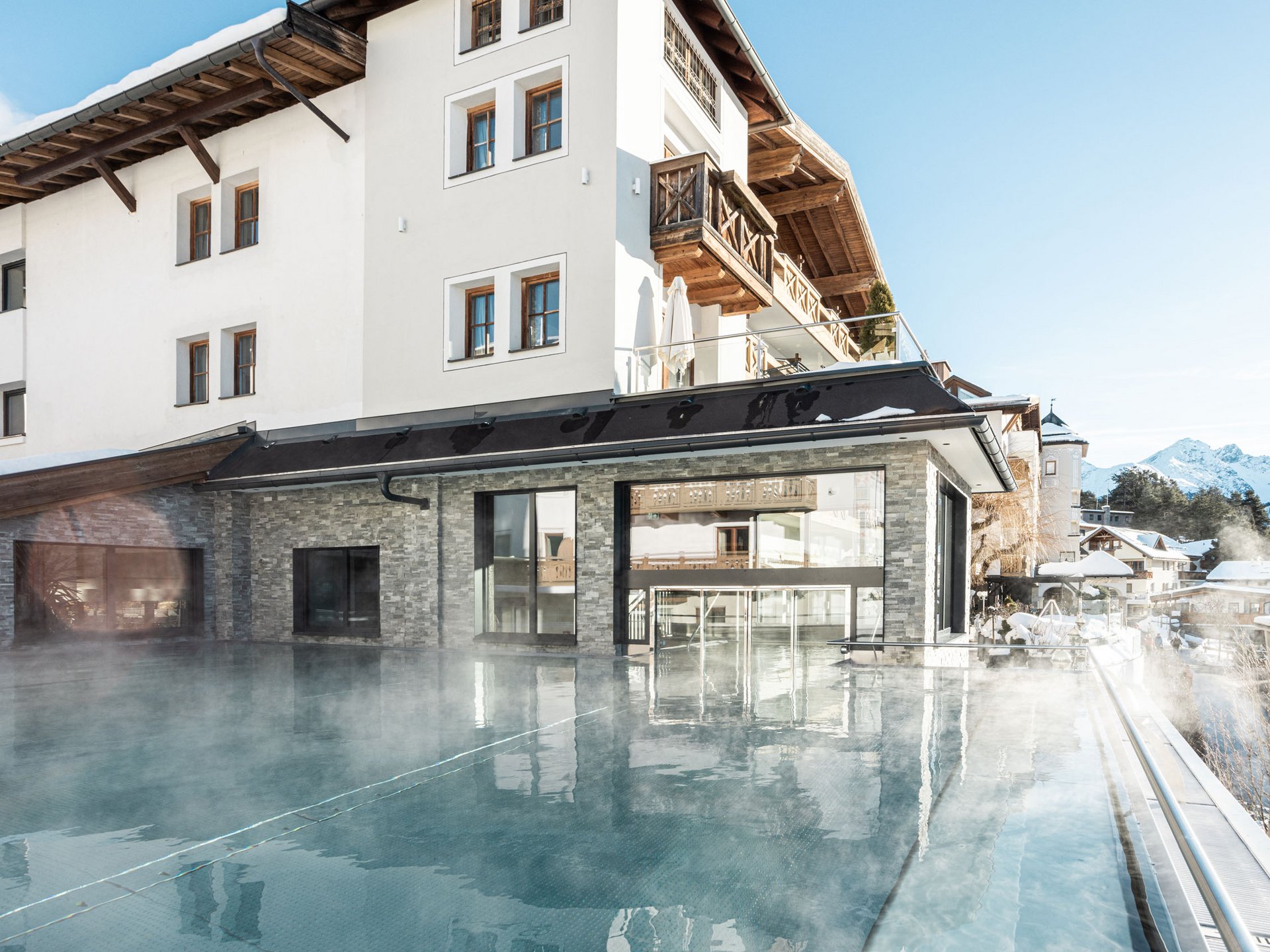 Wohlfühlurlaub im 5-Sterne-Hotel in Serfaus Außenpool mit Dampfwolken neben moderne Berghotel bei Schnee
