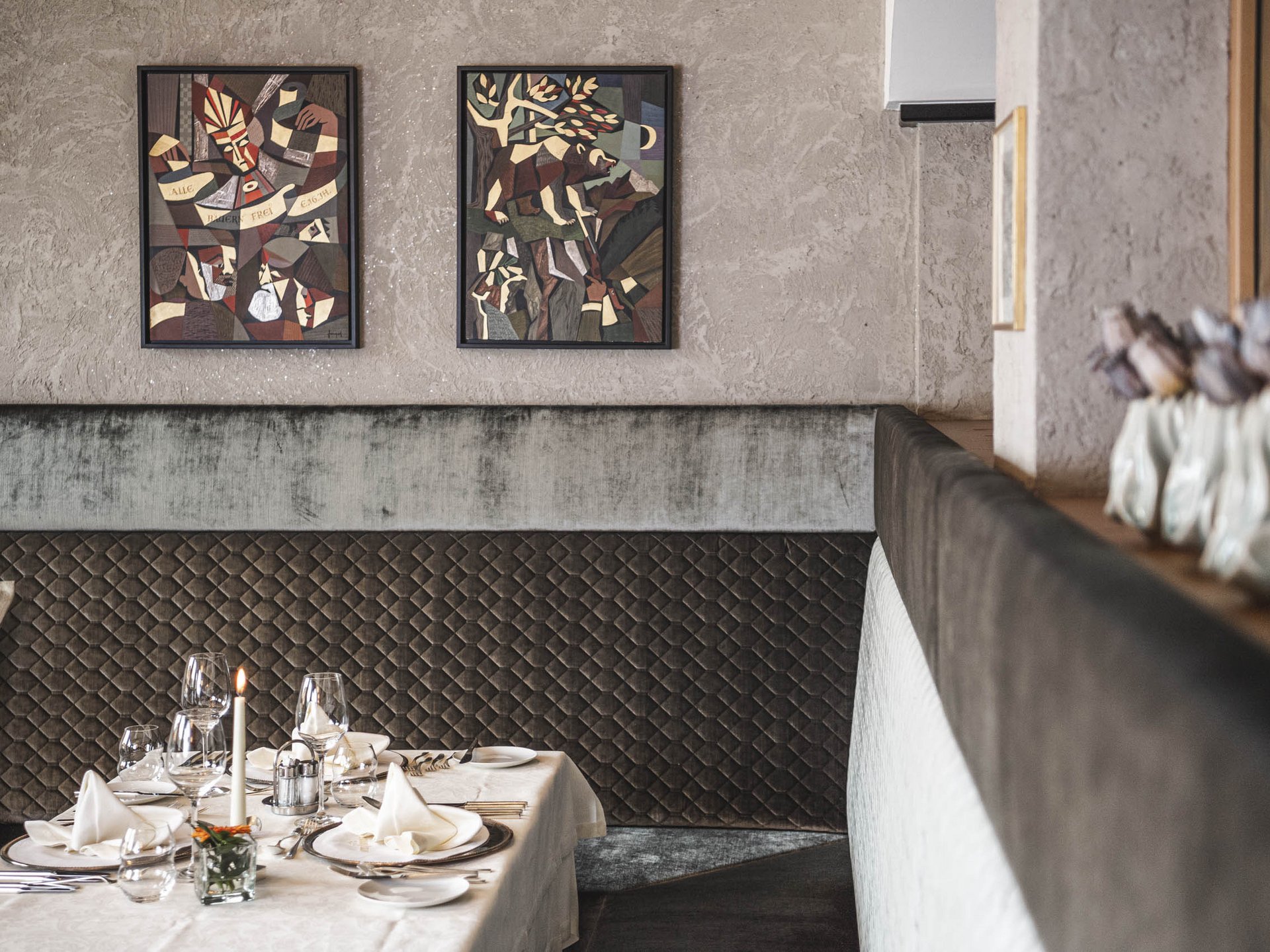 Wohlfühlurlaub im 5-Sterne-Hotel in Serfaus Eleganter gedeckter Tisch mit Kerze vor Kunstwerken und gepolsterter Wand im Restaurant