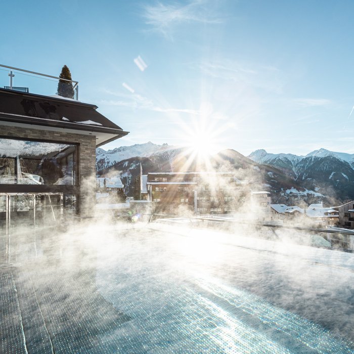 Cervosa – Ihr nachhaltiges Hotel in Österreich Dampfender Außenpool mit Bergblick bei Sonnenaufgang in winterlicher Landschaft