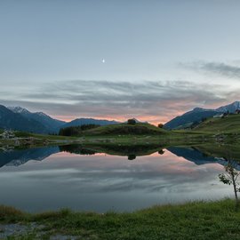 Wohlfühlurlaub im 5-Sterne-Hotel in Serfaus Bergsee spiegelt Hügel und Mond in ruhiger Abenddämmerung