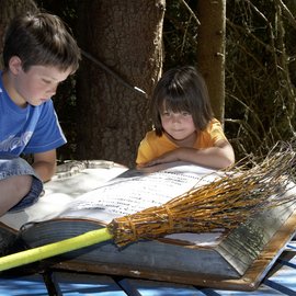 Wohlfühlurlaub im 5-Sterne-Hotel in Serfaus Zwei Kinder lesen ein großes Buch im Wald neben einem Besen