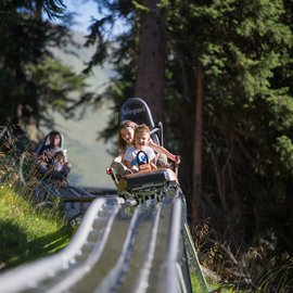 Wohlfühlurlaub im 5-Sterne-Hotel in Serfaus Kinder fahren auf Sommerrodelbahn durch bewaldete Berglandschaft