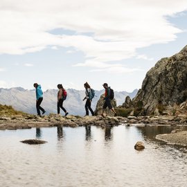 Wohlfühlurlaub im 5-Sterne-Hotel in Serfaus Vier Wanderer mit Rucksäcken auf einem Pfad in den Bergen neben einem See