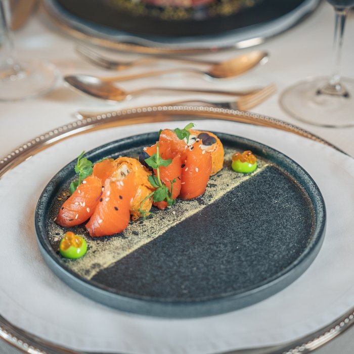 Cervosa – Ihr nachhaltiges Hotel in Österreich Gourmetgericht mit Lachs und grünem Püree auf schwarzem Teller an gedecktem Tisch