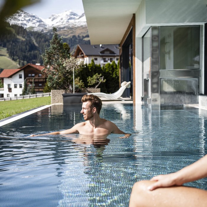 Wohlfühlurlaub im 5-Sterne-Hotel in Serfaus Mann und Frau entspannen im Pool mit Blick auf Berge und Häuser