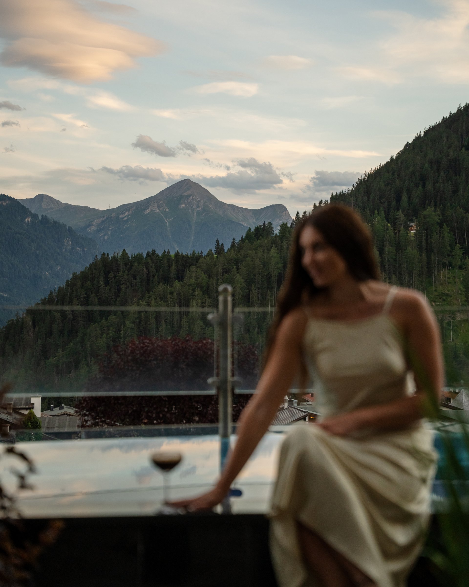Wohlfühlurlaub im 5-Sterne-Hotel in Serfaus Frau in Kleid sitzt neben Pool mit Bergblick bei Sonnenuntergang