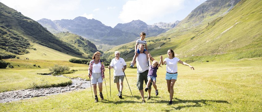 Paragliding and golf holidays in Tyrol Family hiking in green mountains with a creek on a sunny day