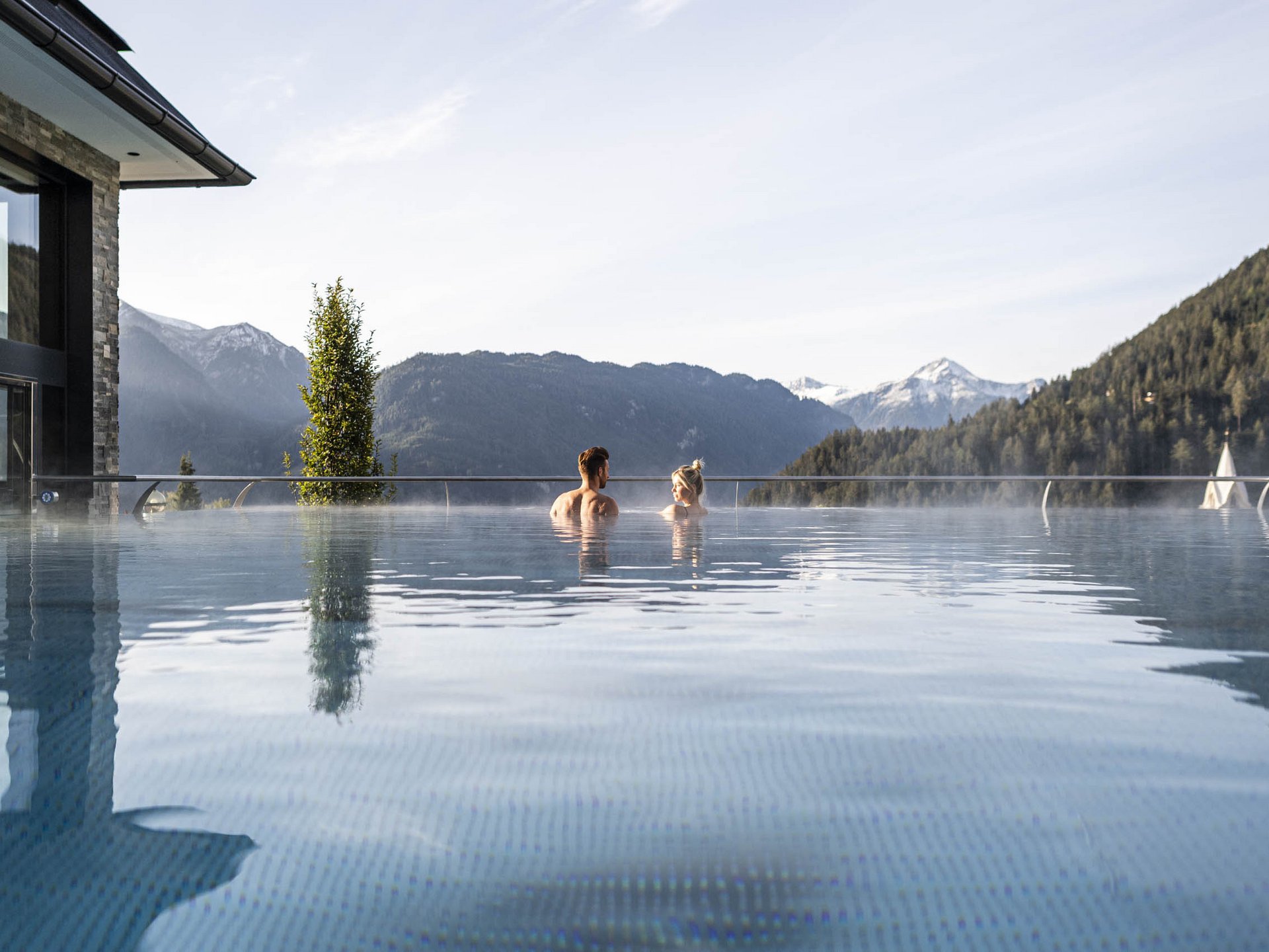 Wohlfühlurlaub im 5-Sterne-Hotel in Serfaus Paar im beheizten Außenpool mit Bergblick und klarem Himmel
