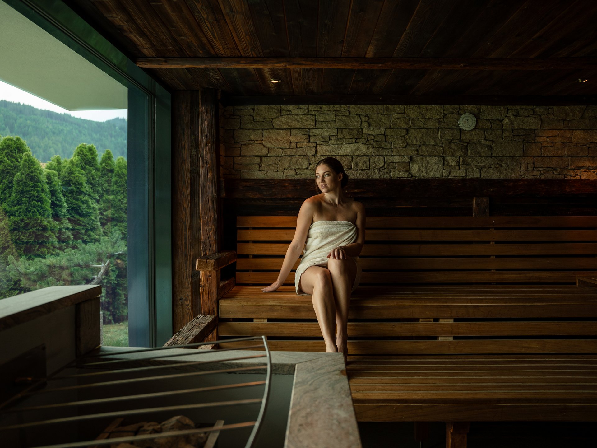 Wohlfühlurlaub im 5-Sterne-Hotel in Serfaus Frau in Handtuch entspannt in Sauna mit Blick auf grüne Bäume