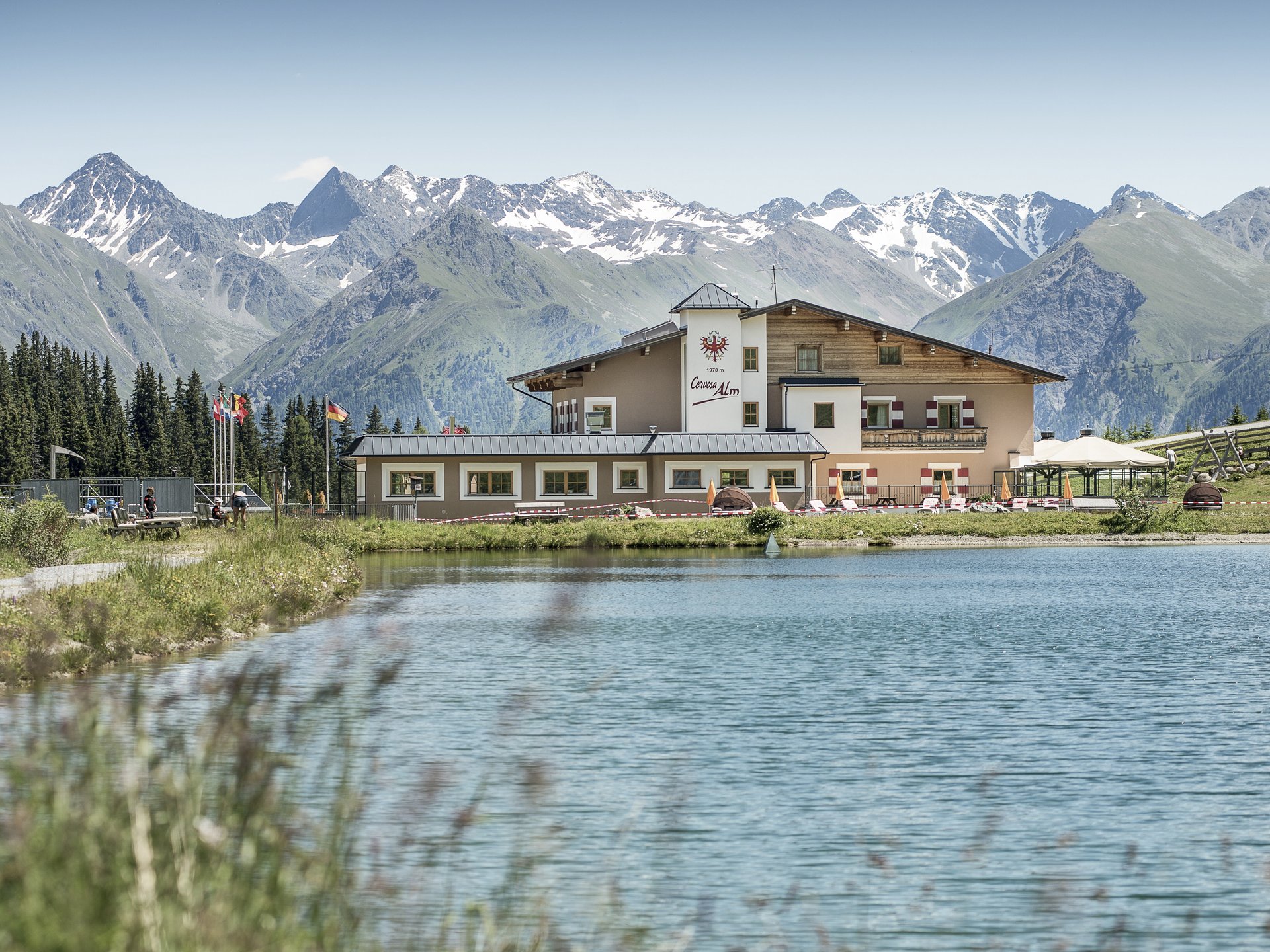 Wohlfühlurlaub im 5-Sterne-Hotel in Serfaus Berghütte am See mit Alpen im Hintergrund bei klarem Himmel