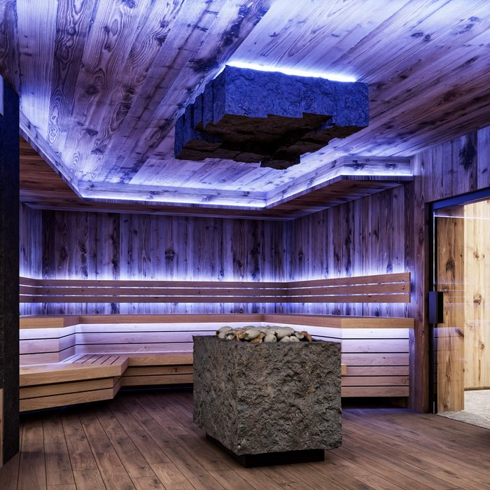 Ligne Mille de luxe facial Modern sauna with wood paneling, stone heater, and indirect blue lighting