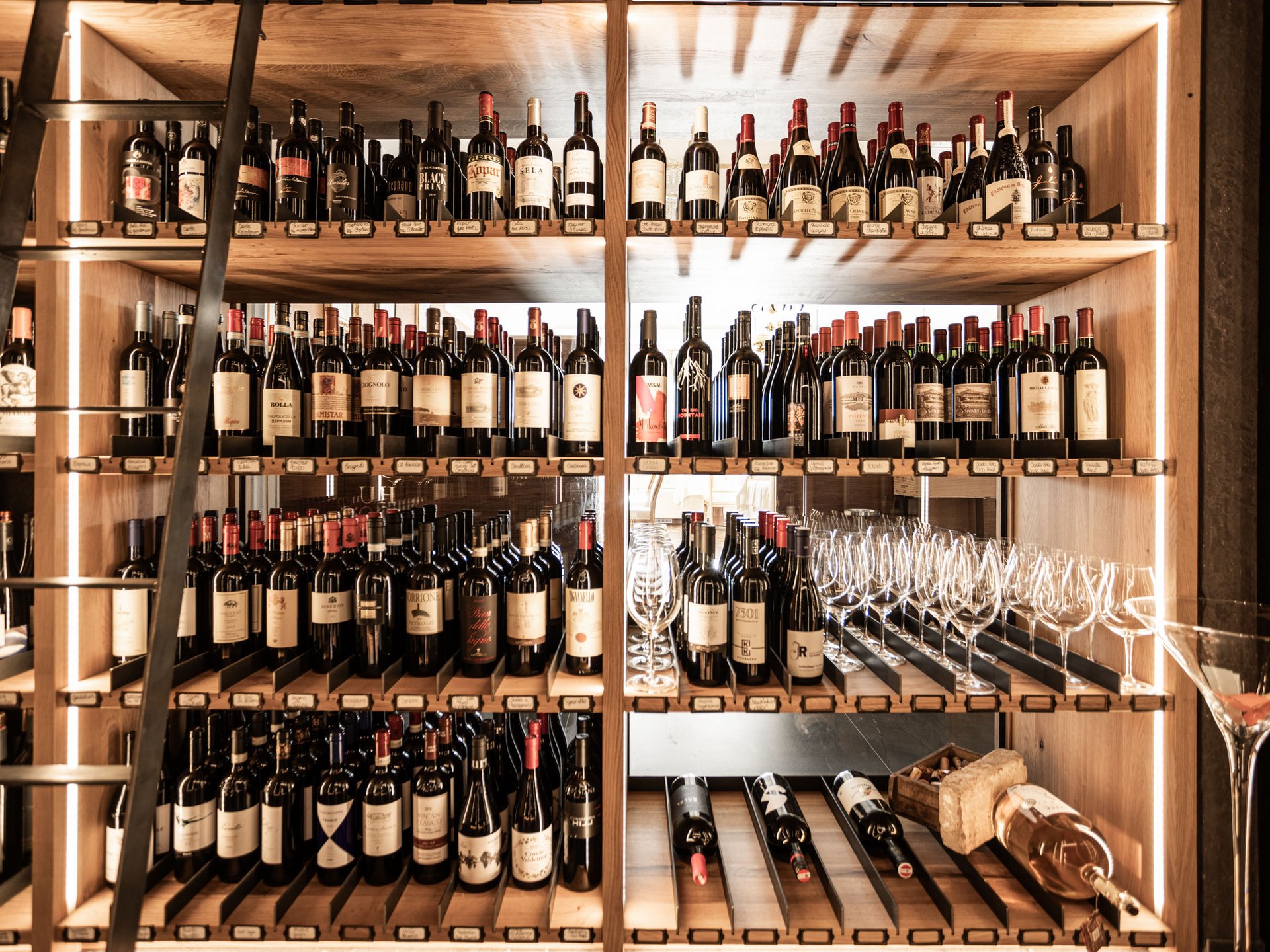 Finest wines and more: wine holiday in Austria at Cervosa Wine rack with many bottles and glasses on wooden shelves