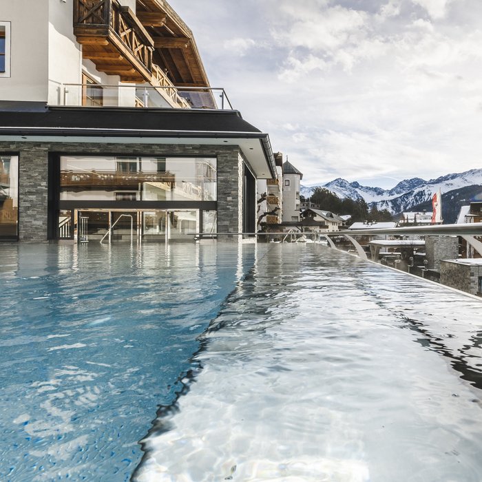 Wohlfühlurlaub im 5-Sterne-Hotel in Serfaus Infinity-Pool mit Bergblick und Sonnenlicht an einem modernen Hotel