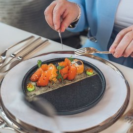 Wohlfühlurlaub im 5-Sterne-Hotel in Serfaus Person isst feines Lachsgericht auf elegantem schwarzen Teller mit Wein