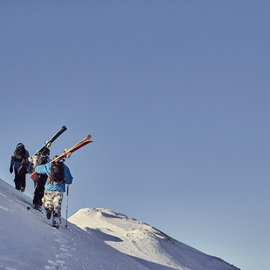 Wohlfühlurlaub im 5-Sterne-Hotel in Serfaus Drei Skifahrer wandern einen schneebedeckten Hang bei klarem Himmel hinauf