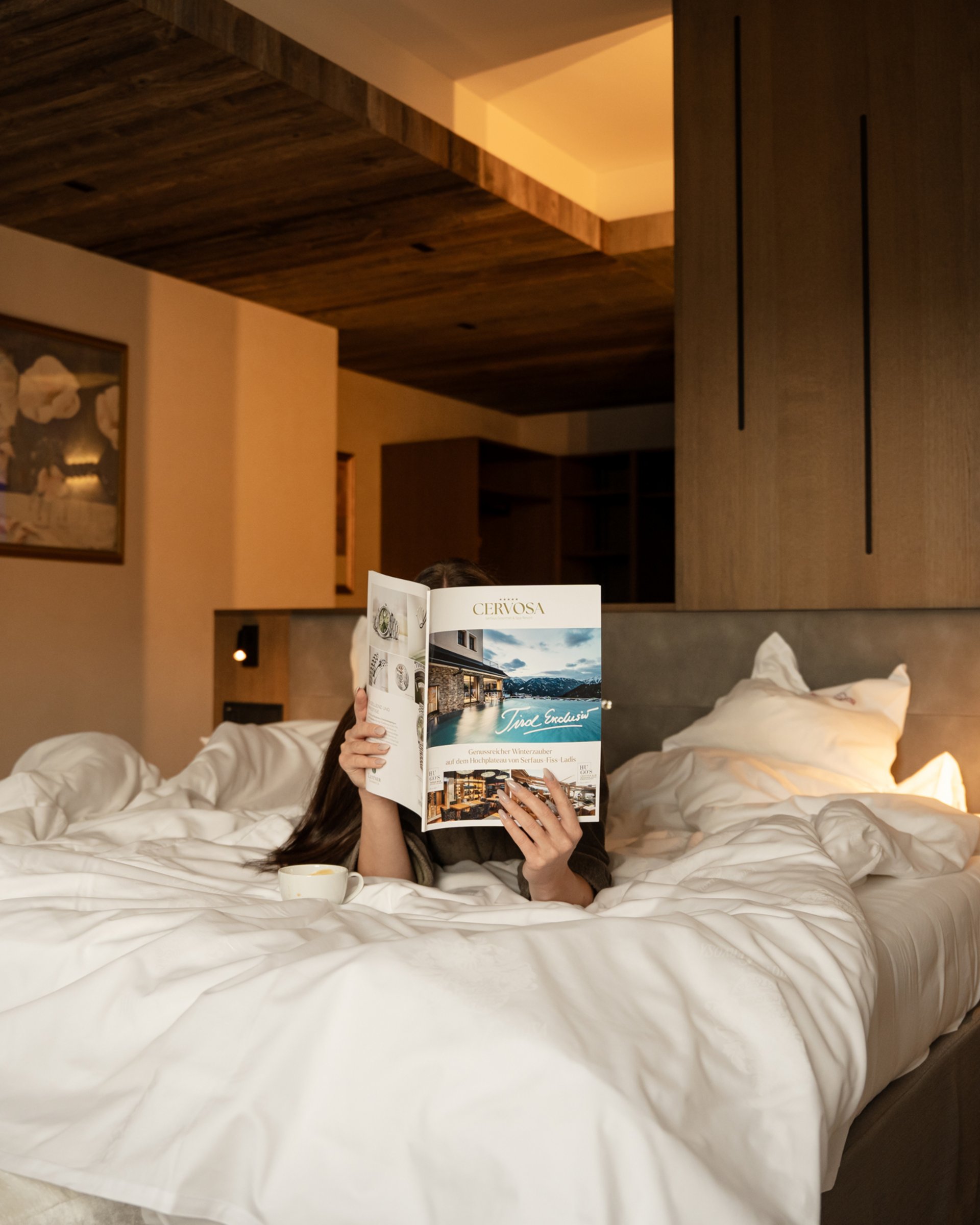 Wohlfühlurlaub im 5-Sterne-Hotel in Serfaus Person liegt im Bett und liest Magazin in einem gemütlichen Hotelzimmer