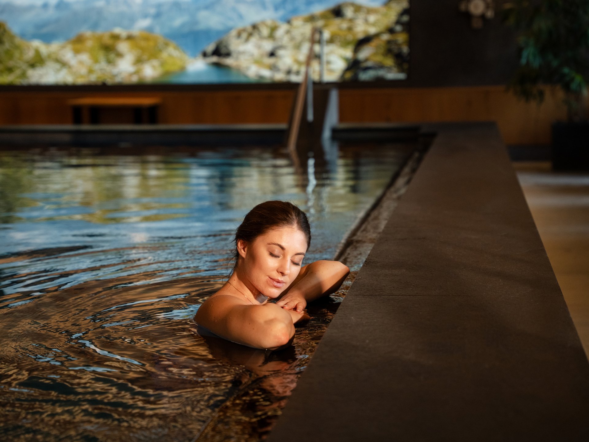 Wohlfühlurlaub im 5-Sterne-Hotel in Serfaus Frau entspannt im Hallenbad mit Berglandschaft im Hintergrund